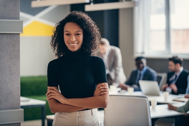 confident african businesswoman smiling at camera while her colleagues working on background