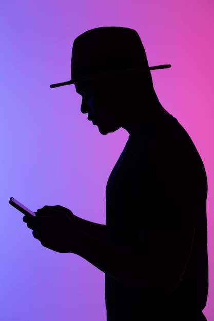 Confident african man silhouette using mobile phone while standing to neon background