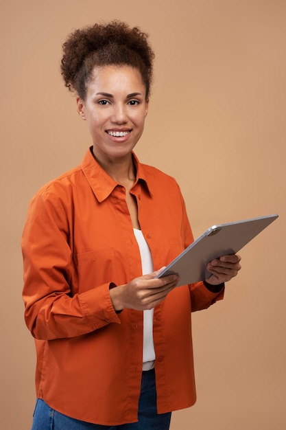 Confident AfricanAmerican woman holding a digital tablet and smiling at camera on beige background