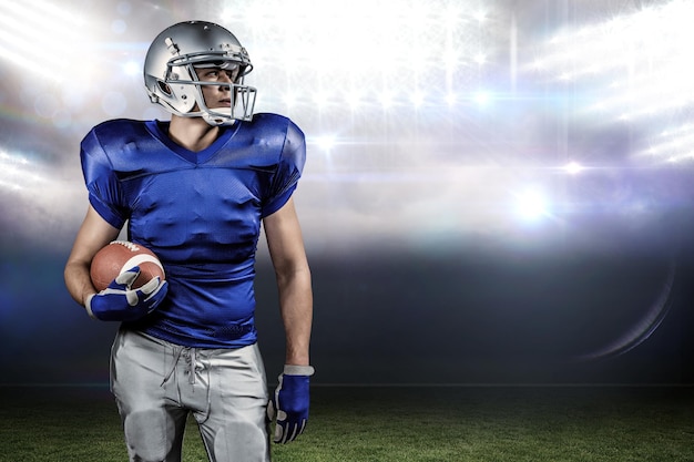 Confident American football player looking away against sports pitch