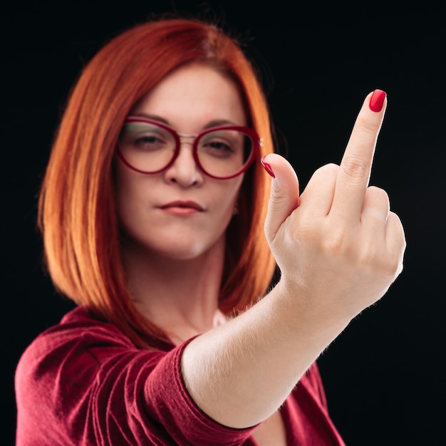 Confident and angry red haired woman showing finger, gesturing fuck off.