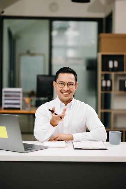 Photo confident asian businessman with a smile standing holding notepad and tablet at the modern office