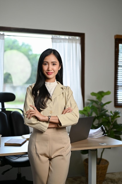 Confident Asian businesswoman arms crossed looking at camera standing in her office