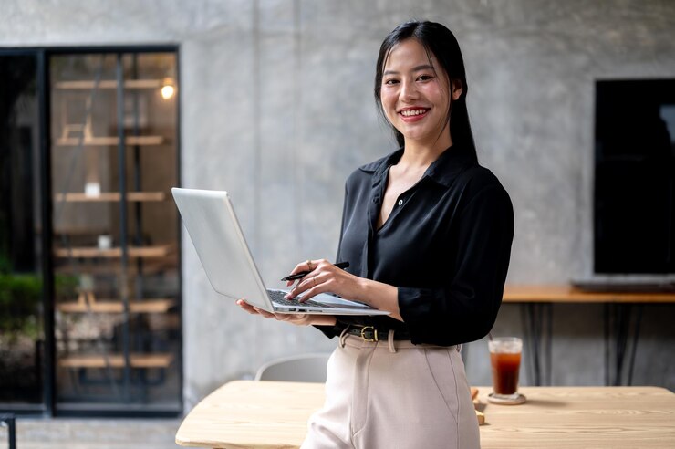 Photo a confident asian businesswoman is standing in her modern loft office with a laptop in her hand
