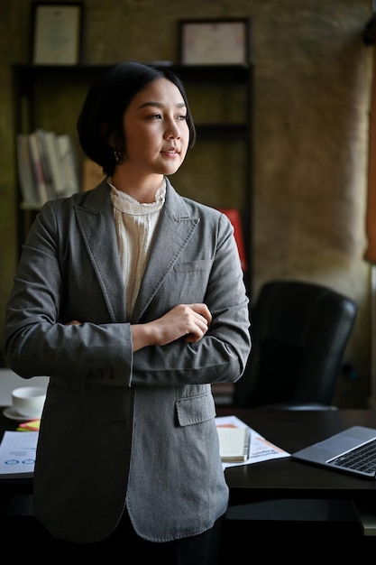 자신감 있는 아시아 사업가가 팔짱을 끼고 사무실에 서 있다