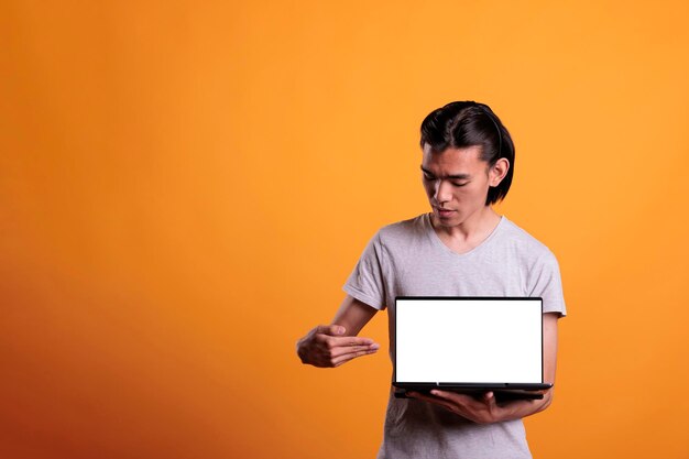 Confident asian man pointing at laptop with white blank screen,\
software advertising mockup with place for text. attractive serious\
person presenting portable computer with empty display