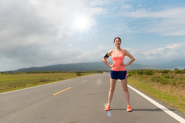 confident asian woman standing on the road ready to running for training endurance in the afternoon of the sunny day with beautiful scenery background over blank copyspace.