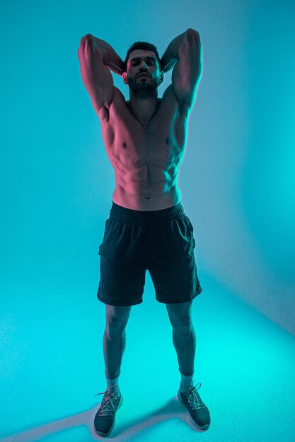 Confident athletic bearded european young man. Front view of guy with naked sportive torso and looking at camera. Isolated on blue background. Studio shoot