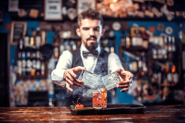 Confident barman adds ingredients to a cocktail while standing near the bar counter in nightclub