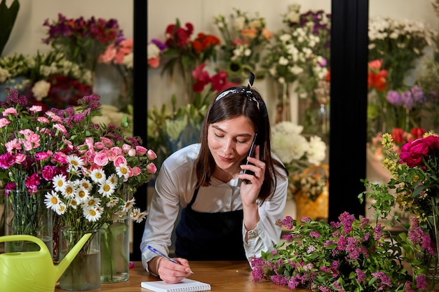 Confident beautiful flower shop owner talking on phone with\
client. small business.