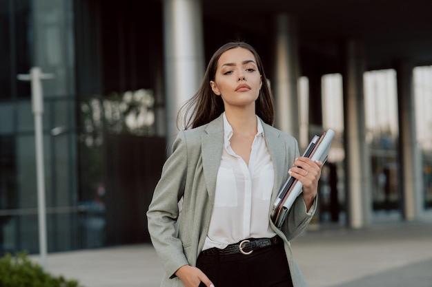 Confident beautiful woman leaves work in afternoon in\
background glass modern building