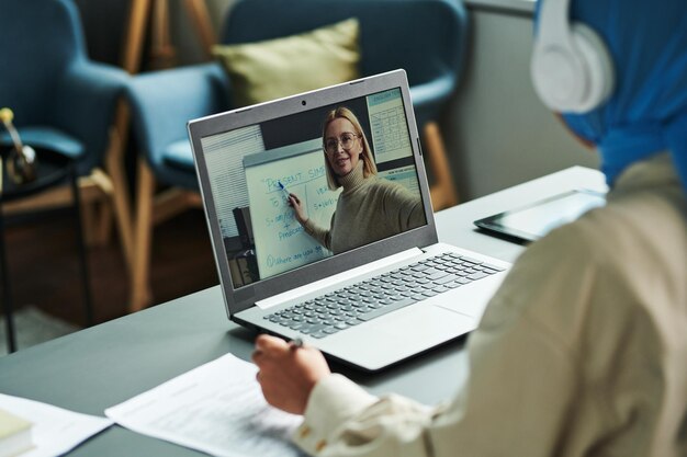 Confident blond teacher on laptop screen pointing at whiteboard