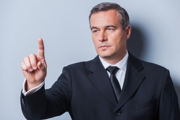 Confident business expert. Confident mature man in formalwear looking at camera and keeping arms crossed while standing against grey background