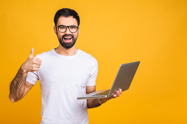 Esperto di affari fiducioso. fiducioso giovane uomo bello in casual azienda laptop e sorridente mentre in piedi isolato su sfondo giallo. pollice su.