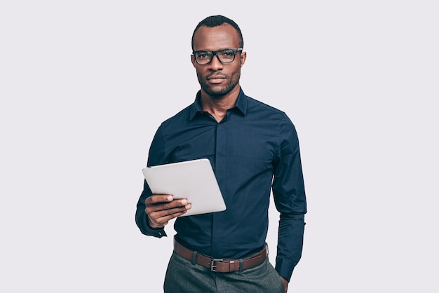 자신감 있는 비즈니스 전문가. 디지털 태블릿을 들고 서 있는 동안 카메라를 보고 있는 잘생긴 젊은 아프리카 남자