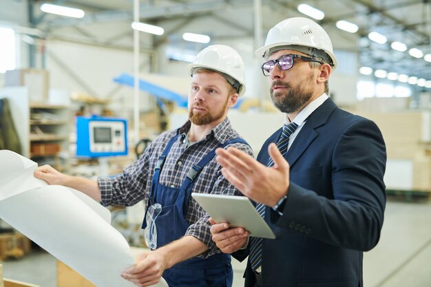 Confident business investor visiting factory and talking to engi