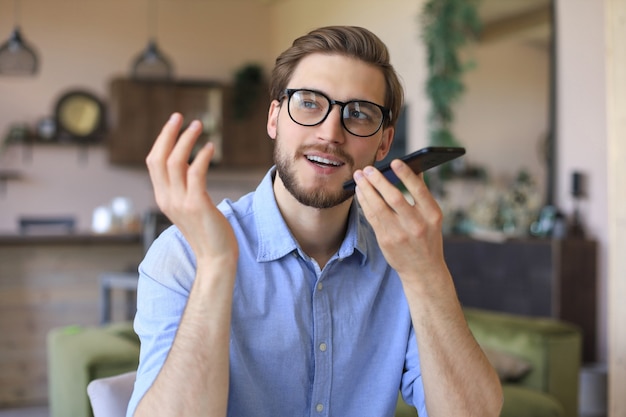 Foto uomo d'affari sicuro con gli occhiali che tiene lo smartphone vicino alla bocca per registrare messaggi vocali o attivare l'assistente digitale.