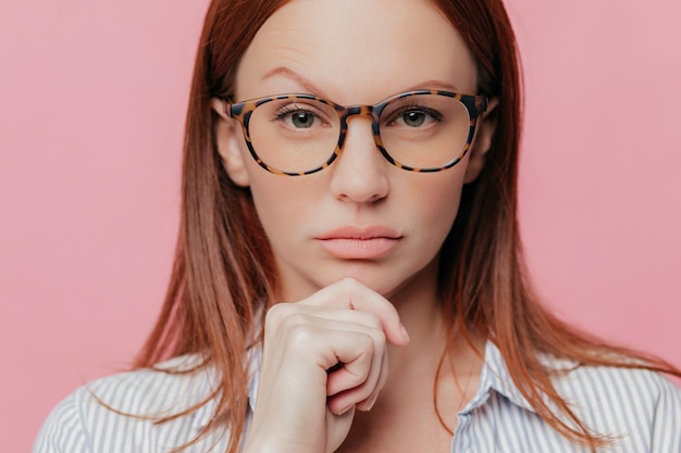 Photo confident business owner chin in hand raised eyebrow optical glasses dark hair elegant shirt serious gaze studio shot