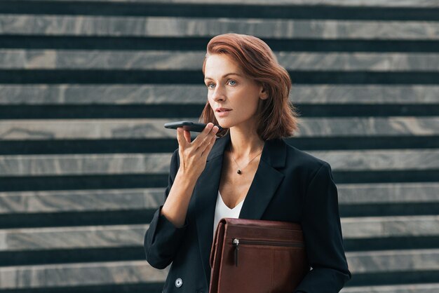 Photo confident business woman recording voice message while standing outdoors