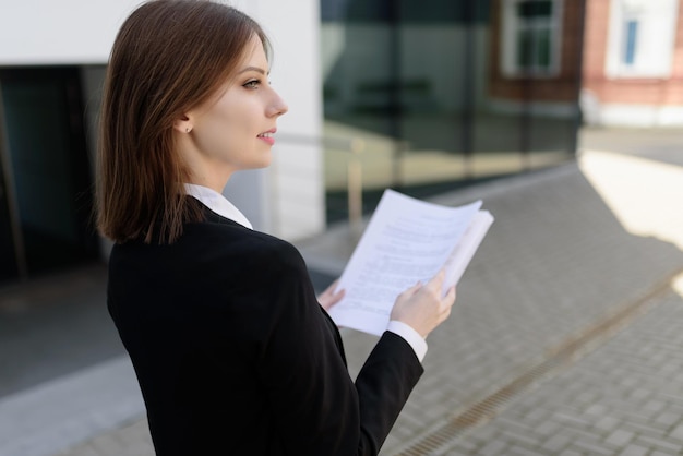 A confident business woman stands with documents near the business center