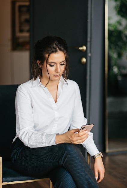 Confident business woman in a white shirt and trousers holds a smartphone in her hands