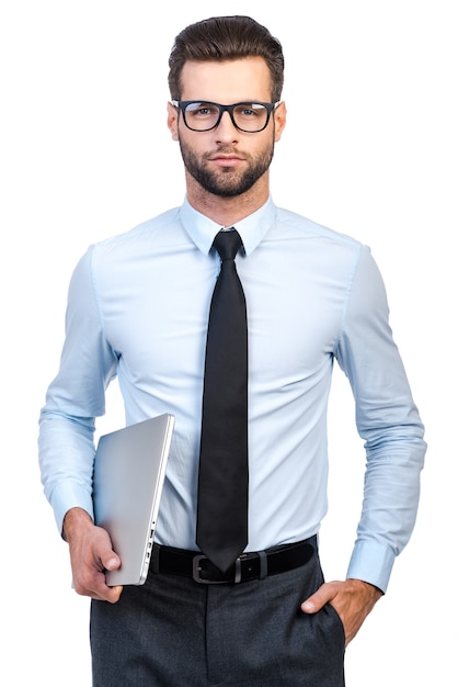 Confident businessman. Confident young handsome man in shirt and tie carrying laptop and looking at camera while standing against white background