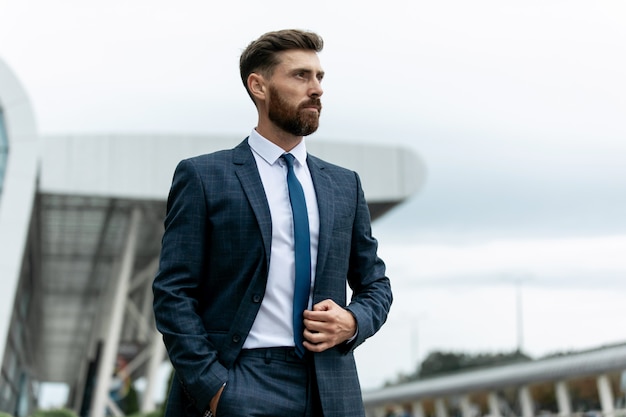 Confident businessman. Confident young man in full suit adjusting his sleeve and looking away while standing outdoors with cityscape in the background