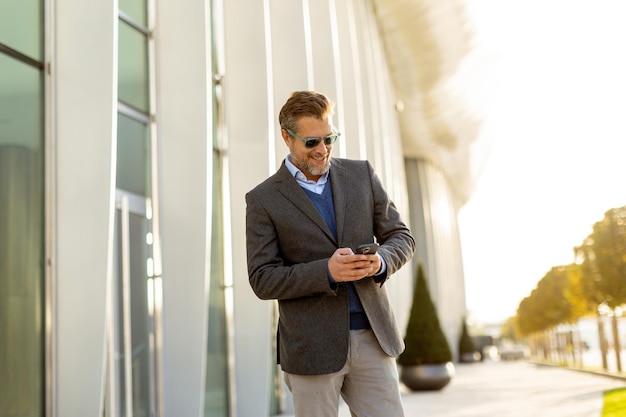 confident businessman enjoys a sunny afternoon while checking his phone near a modern building