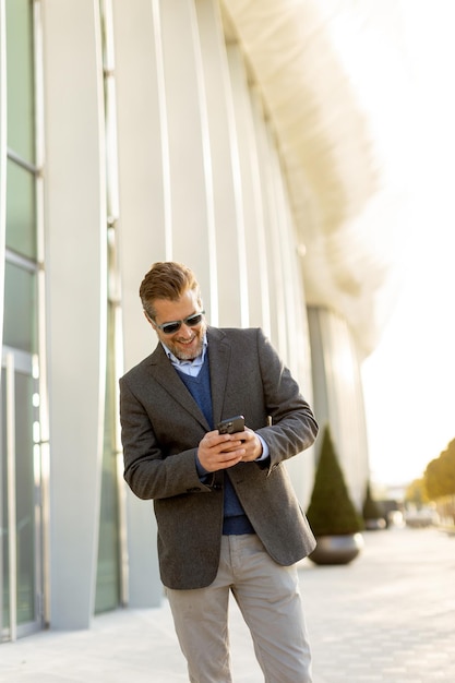 confident businessman enjoys a sunny afternoon while checking his phone near a modern building