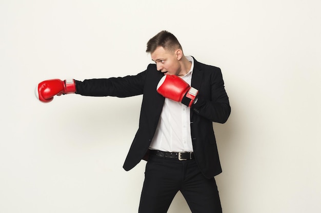 Confident businessman in red boxing gloves punch to the goal. Ready to fight in corporate battle, business competition and perseverance concept, white studio background