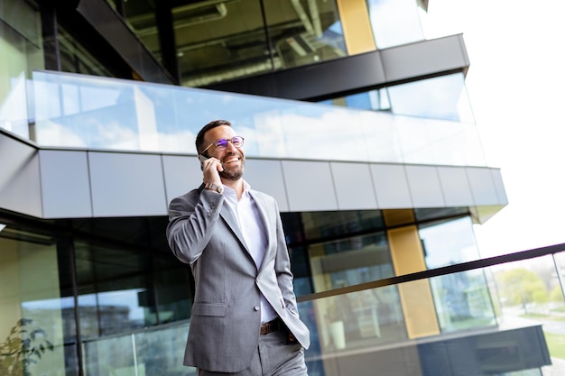 Confident Businessman Smiling in Sharp Suit Against Modern Glass Office Facade