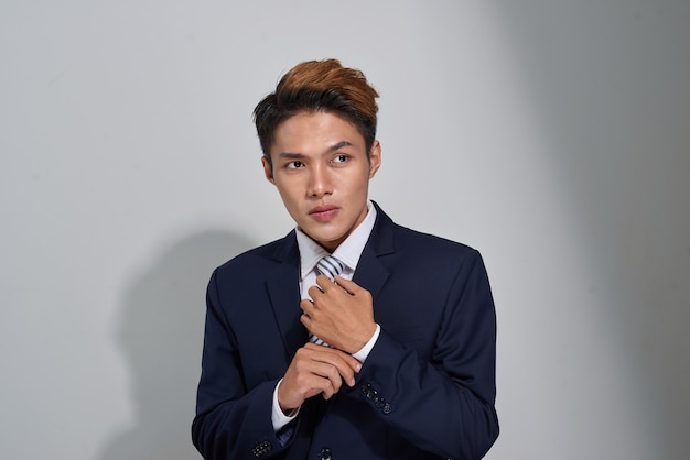 Confident businessman straightening his tie over gray background and looking at camera