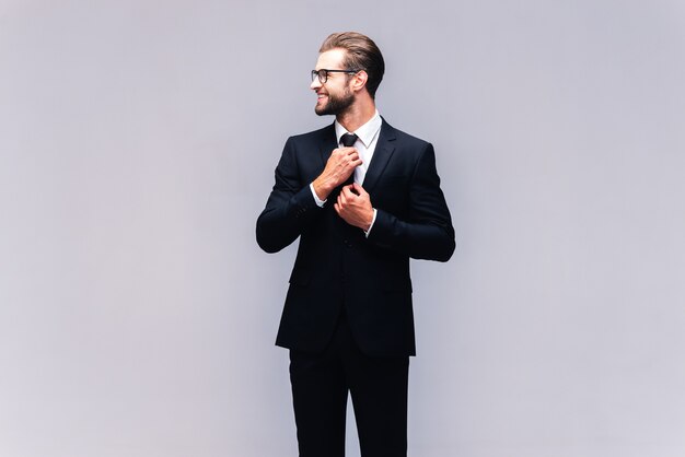 Confident businessman. Studio shot of handsome young man in full suit adjusting his necktie and smiling