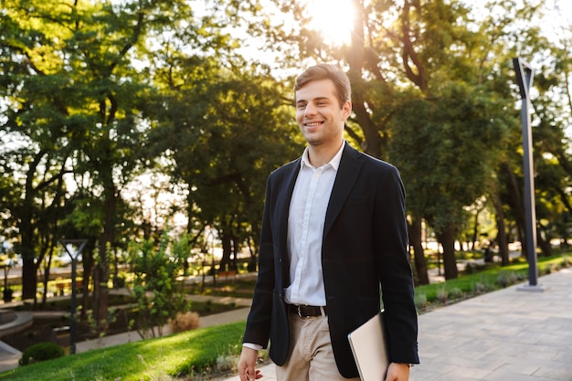 Confident businessman walking outdoors, carrying a laptop