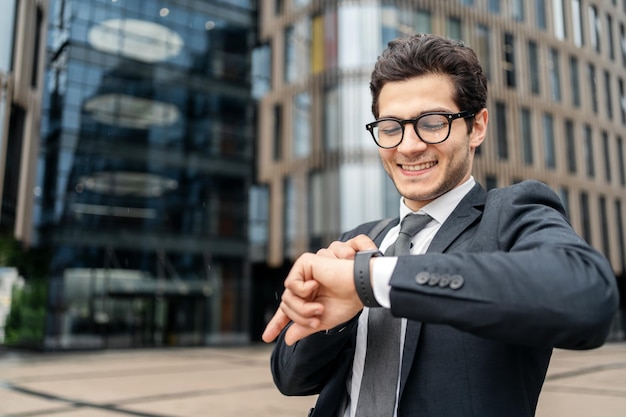 A confident businessman with cheerful glasses looks at his watch for work in a business suit