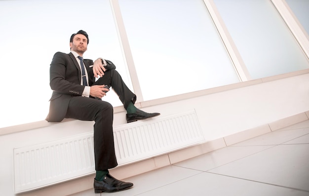 Confident businessman with a smartphone sitting in the office hallway