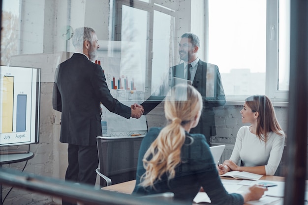 Confident businessmen shaking hands and smiling while working together with colleagues in the board room