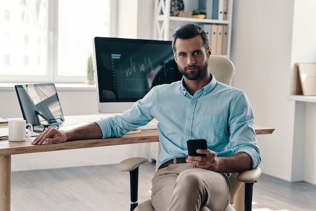 Confident businessmen. Young modern businessman looking at camera while sitting in the office