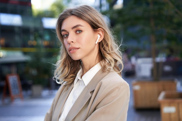 Confident businesswoman in headphones and beige suit looking at camera with thoughtful gaze posing o