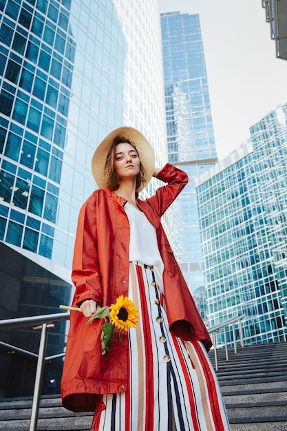 Confident businesswoman is awaiting meeting or date woman in fashion clothes with sunflower is standing in financial centre Businesswoman concept of being yourself stay close to nature in city