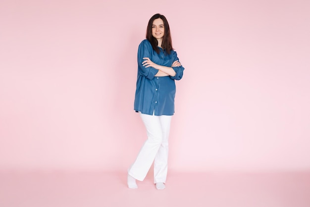 Confident businesswoman in stylish smart casual outfit standing with folded hands isolated on pink background full body shot