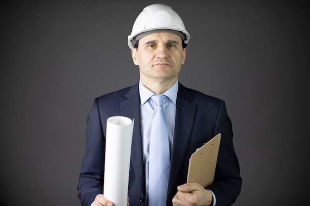 Photo confident and calm builder in white helmet holds rolled-up drawing and clipboard