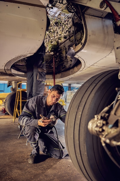 Confident Caucasian mechanic working at an airplane hangar and fixing the landing gear of a plane