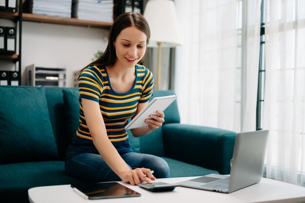 Confident caucasian woman with a smile standing holding notepad and tablet in living room on the sofa at home office