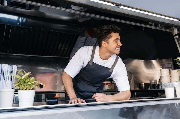 Confident chef in food truck leaning counter Young food truck owner waiting for customers