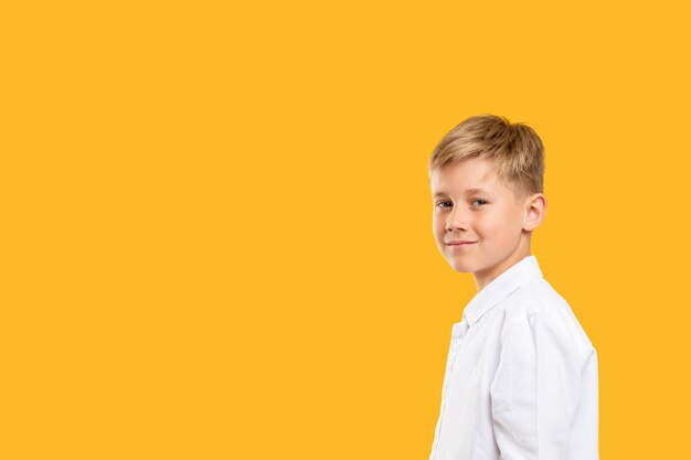 Confident child portrait. Back to school. Smart boy in white shirt smiling isolated on orange copy space.