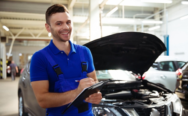 Confident and concentrated young and experienced car repair specialist with a tablet in his hand inspects and diagnosis the car for breakdowns