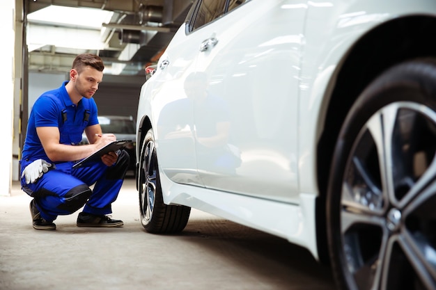 Confident and concentrated young and experienced car repair specialist with a tablet in his hand inspects and diagnosis the car for breakdowns