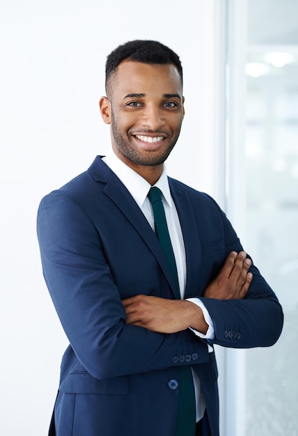 Photo confident corporate charm a handsome young african american businessman standing indoors with his arms folded