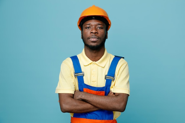 Confident crossing hands young african american builder in uniform isolated on blue background